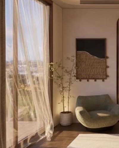 Sage lounge chair beside a tall window with sheer curtains and a potted tree.