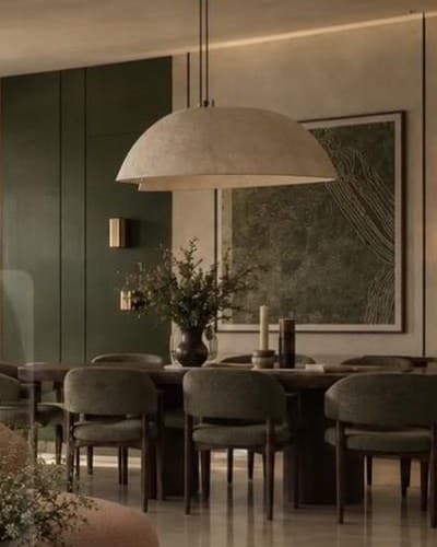 Dining table with olive upholstered chairs against a deep olive panelled wall, under a textured dome pendant.