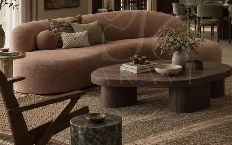 Curved clay-pink bouclé sofa with patterned cushions behind a low organic timber coffee table.