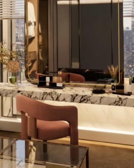 Close view of the marble vanity with a rust bouclé chair and the lower edge of the rounded mirror.